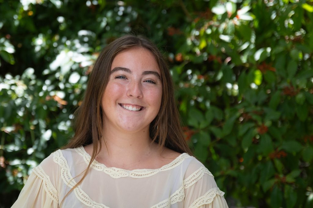 Student standing before bushes dappled with sunlight