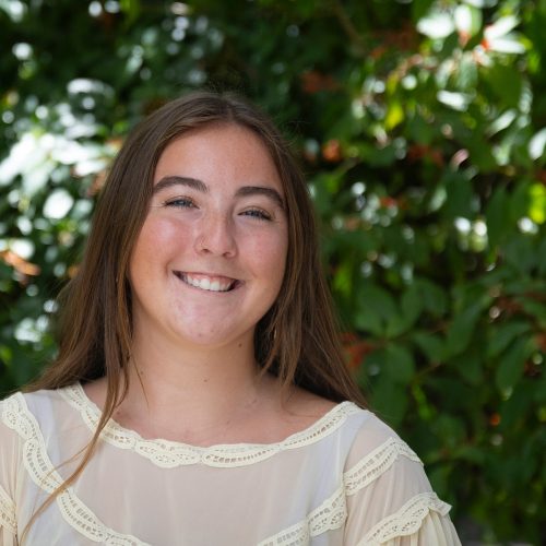 Student standing before bushes dappled with sunlight