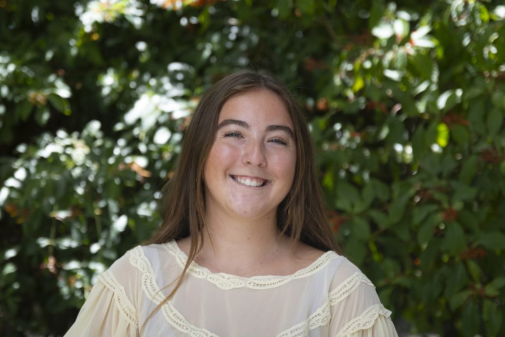 Student standing before bushes dappled with sunlight