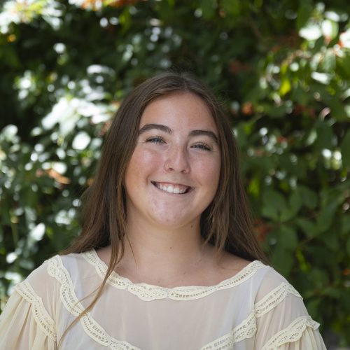 Student standing before bushes dappled with sunlight