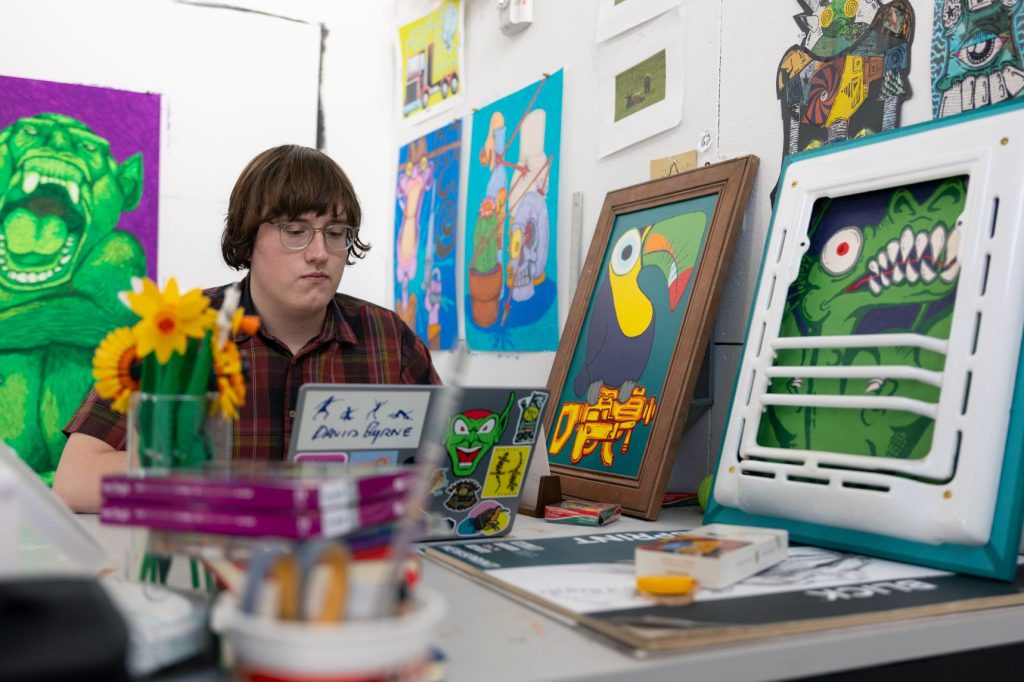 A student sits in an art studio surrounded by vibrantly colorful works of art.
