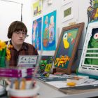 A student sits in an art studio surrounded by vibrantly colorful works of art.