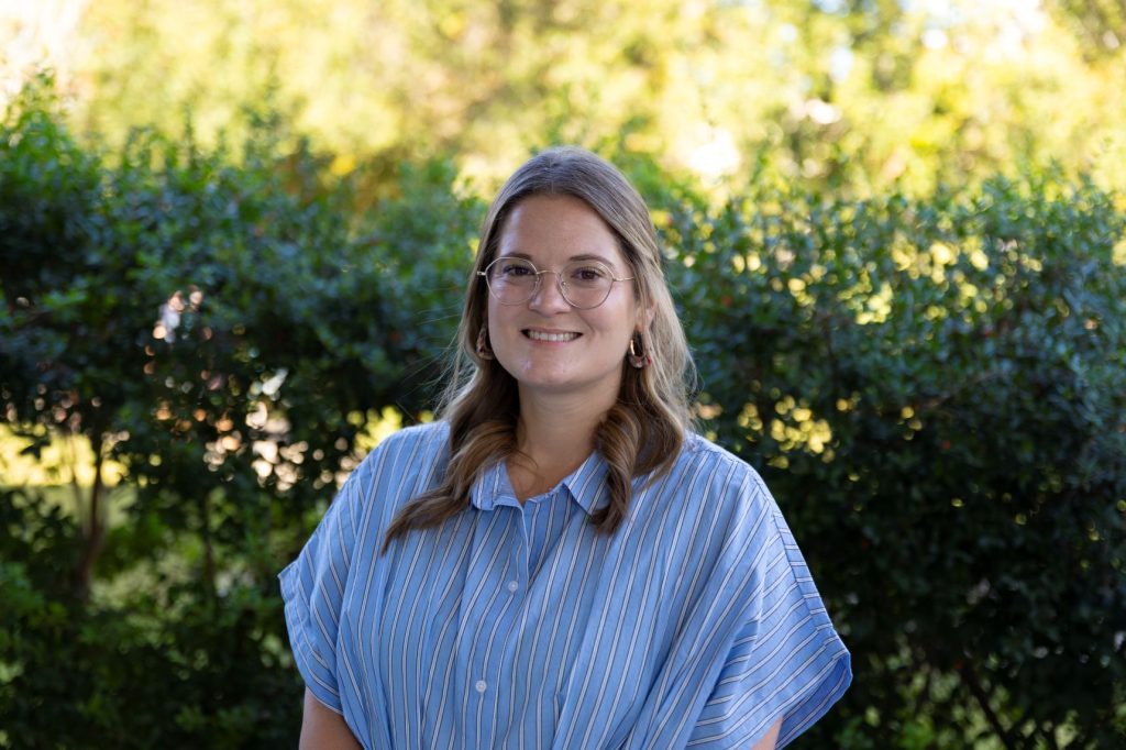 A woman wearing a blue shirt with white stripes and glasses on.