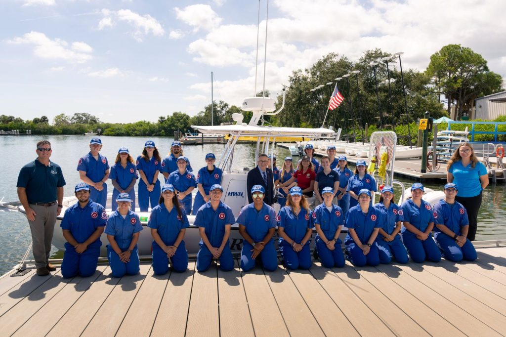 A large group of people, with some standing in a boat and others sitting on a pier.