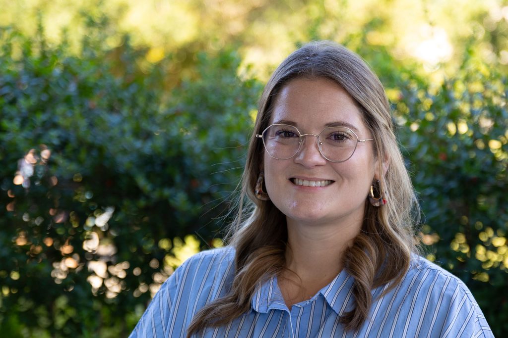 A woman wearing a blue shirt with white stripes and glasses on.