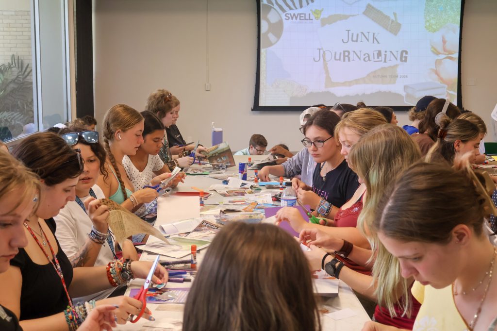 A long table surrounded by a large group of students working on crafts with scissors, construction paper, glue