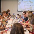 A long table surrounded by a large group of students working on crafts with scissors, construction paper, glue