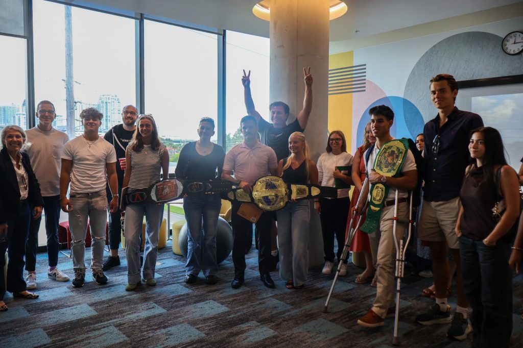 A group of college students stands together in a group in a well lit room.