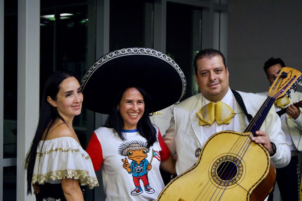Two women, one with a giant sombrero on, and a man holding a guitar.