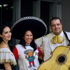 Two women, one with a giant sombrero on, and a man holding a guitar.