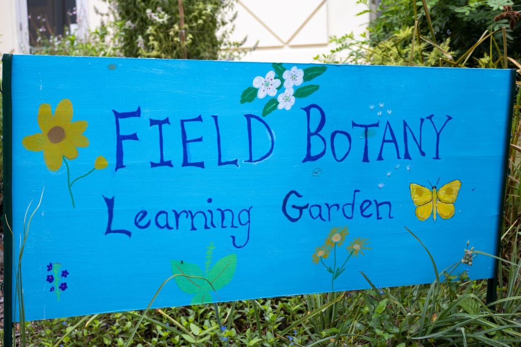 A blue sign says "Field Botany Learning Garden" on it.