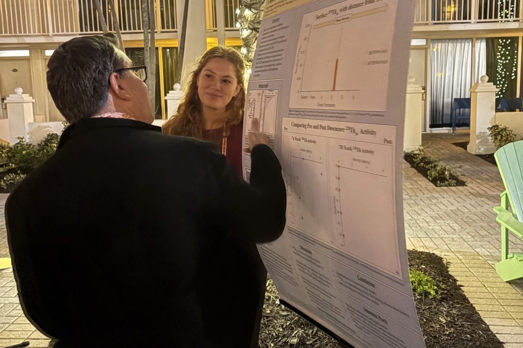 A person in a black suit jacket examines a poster as a young woman looks on.