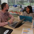 A man sides in front of a laptop computer with a young woman, also near a laptop, sits to his left.