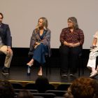 Four people sit on a stage and the one on the far left is speaking into a microphone.