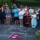 A group of people hold a candlelight vigil over a chalk drawing that reads "Pray for Nepal."