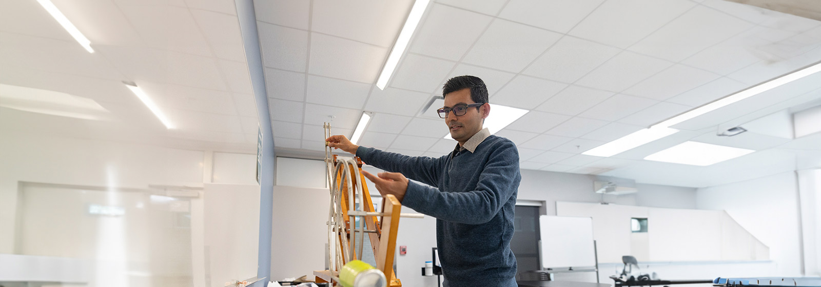 Professor wearing glasses holds a physics instrument containing an aluminum can