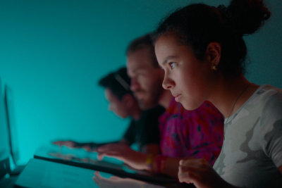 Three students seated next to each and looking intensely at computer screens