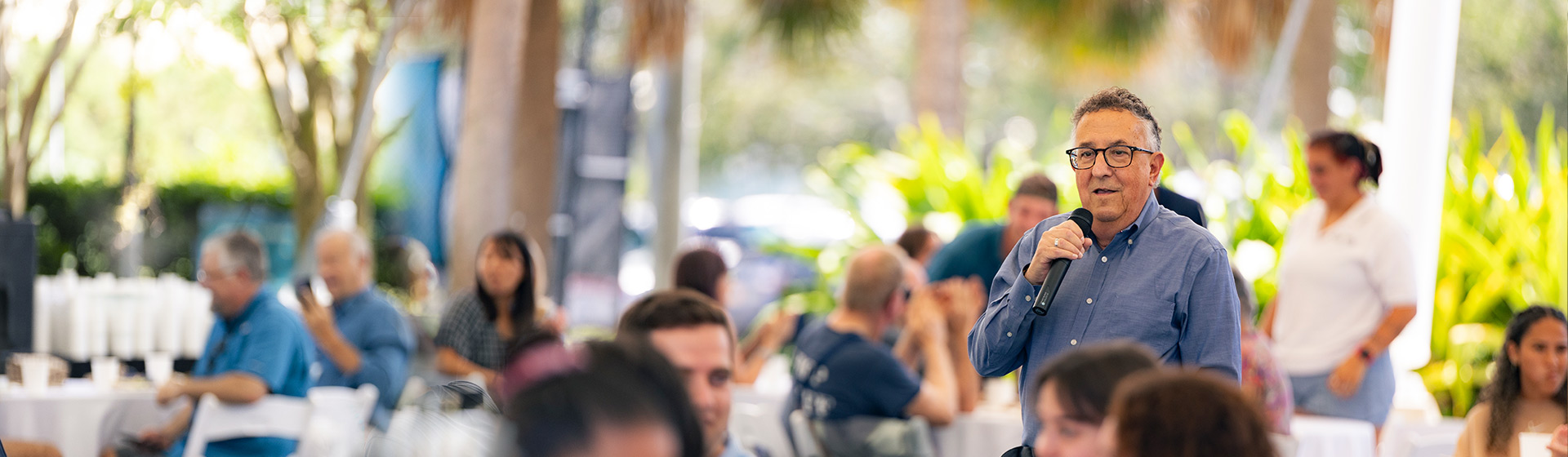 President Annarelli speaks to crowd with handheld microphone at covered, outdoor venue