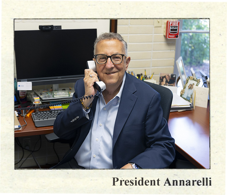 Gentleman in shirt and jacket at desk smiles while holding phone to ear