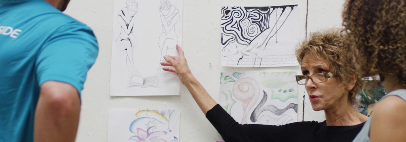 Visual Arts instructor Betsy Lester pointing to artwork on board as students listen