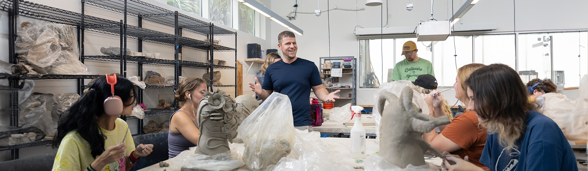 Visual Arts professor teaching ceramics to a group of students seated at an art table working on their clay sculptures