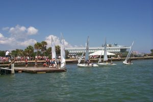 Students on the docks of the boathouse while sailboats stream by