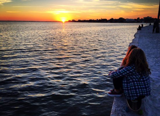 Students sitting on seawall watch a sunset