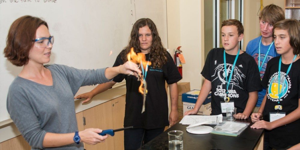 Summer Science Splash campers look on while a professor conducts an experiment in which she burns a dollar bill