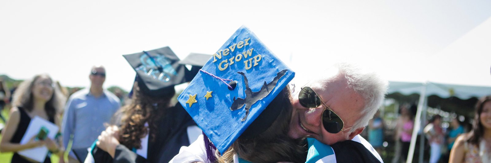 Parent hugging graduate with a cap that says "Never Grow Up"