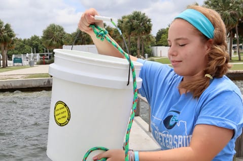 Student holding bucket of sea water off pier
