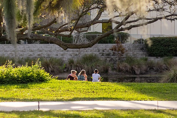 Eckerd students seated along pond by James Center