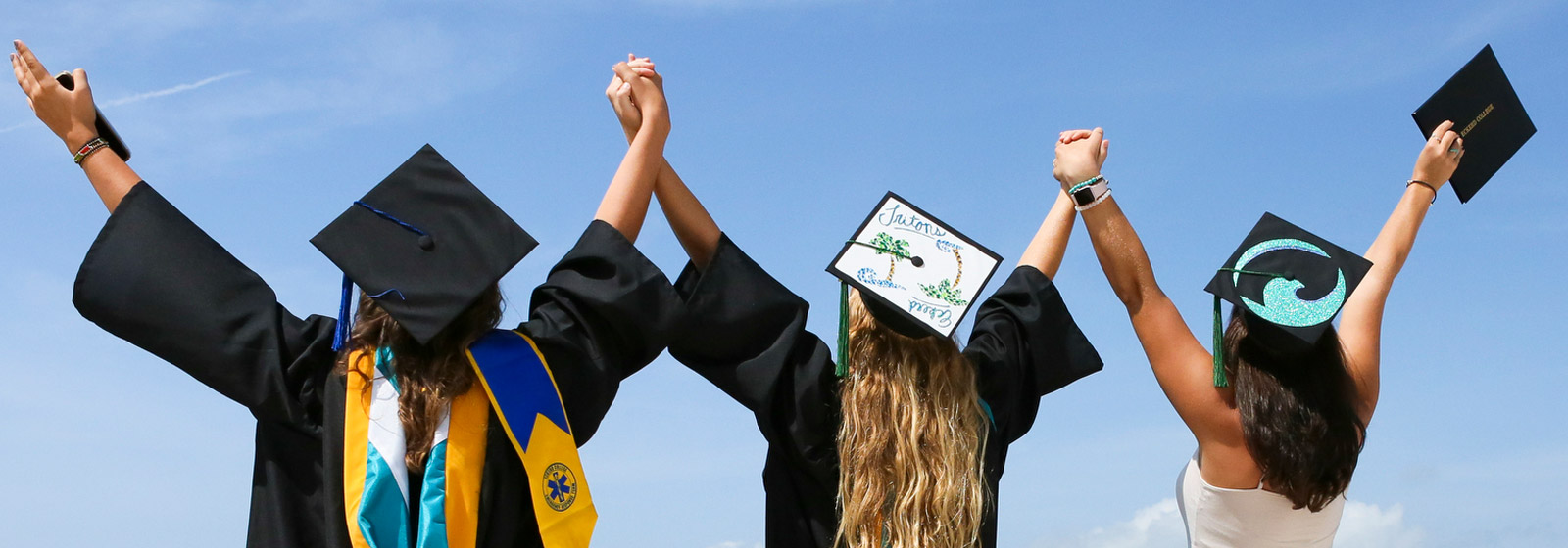 Students holding upraised hands, looking out over the bay holding diplomas