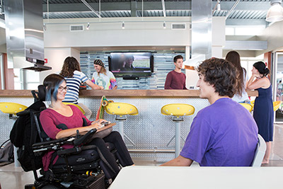 Student in wheelchair chats with student in chair at a student lounge