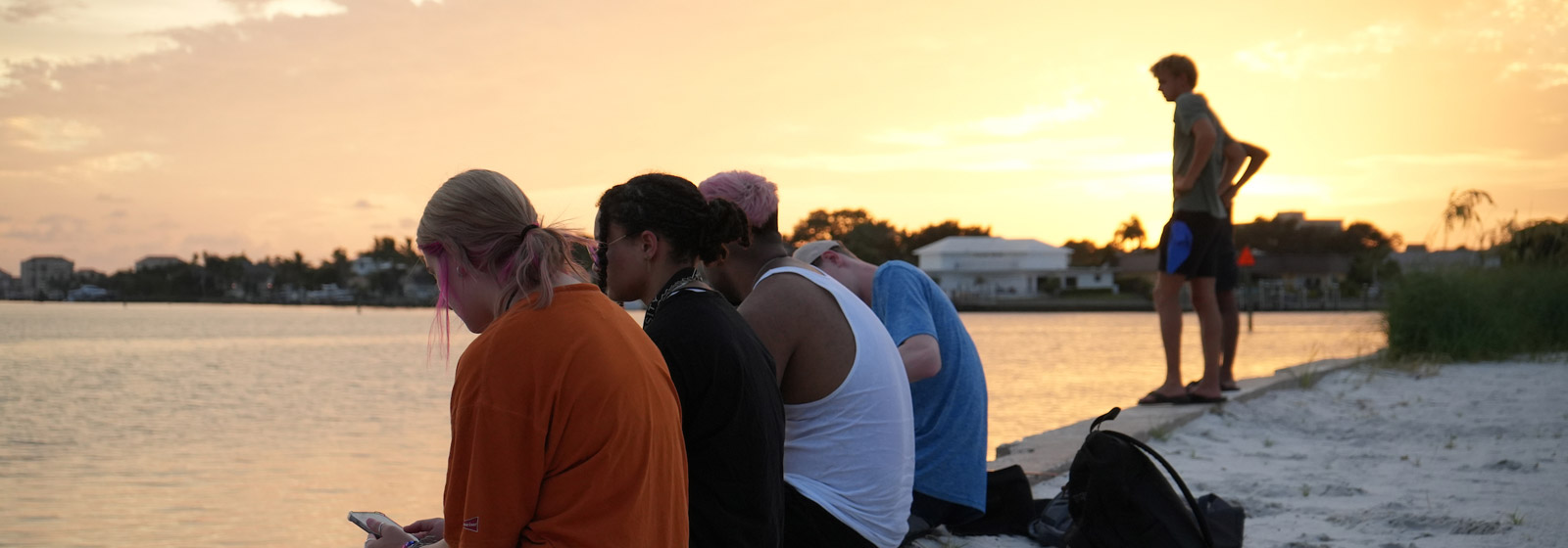 Eckerd College students sit along the seawall at sunset