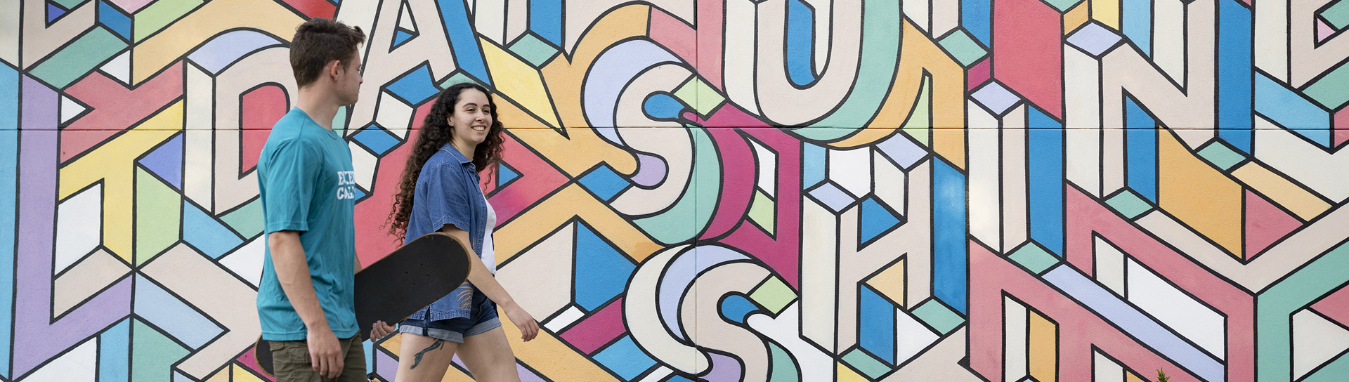 Eckerd students walking with skateboard walking paste a mural in downtown St. Petersburg