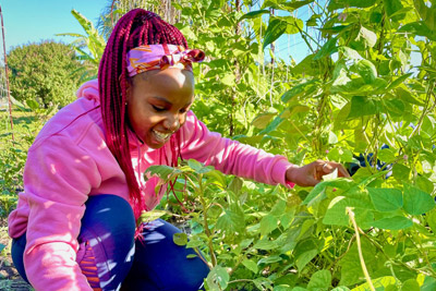 Student with red hair squatting by row of plants