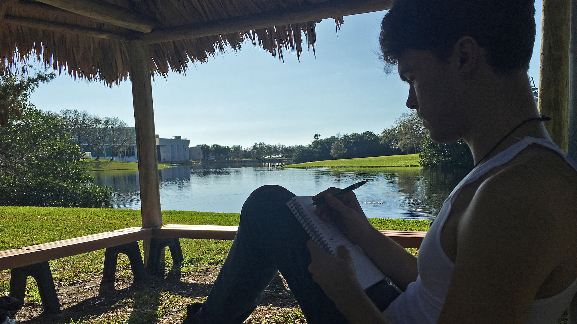 Student seated under chickee while writing in notebook