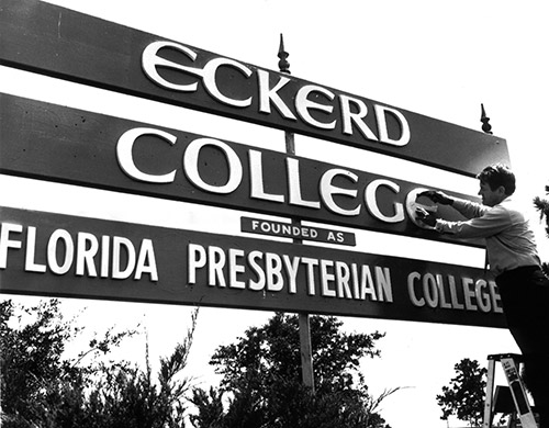 Black and white photo of man on a ladder adding the letter "e" to a sign that says "Eckerd College founded as Florida Presbyterian College"