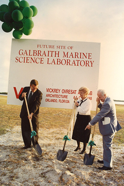 Two men and a woman in formal attire use shovels to break ground next to sign that reads Galbraith Marine Science Laboratory