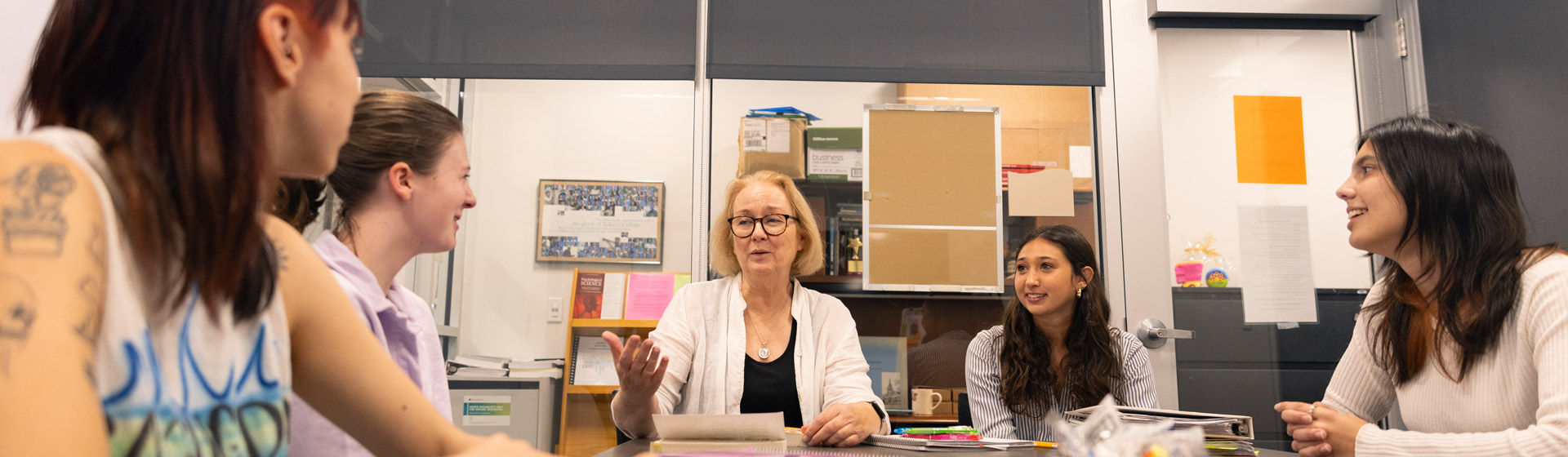 Staff member wearing glasses sits at a large table with another coach and three students