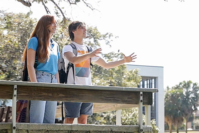 Two students wearing backpacks chatting while looking out over a body of water