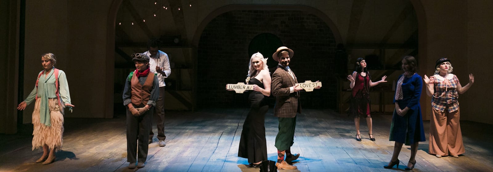 Eight Theatre students stand on stage holding signs "Love St" and "Lumber Ave"
