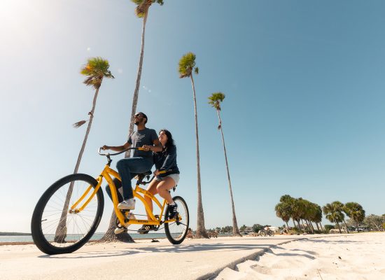Eckerd students ride a tandem yellow bike along the beach