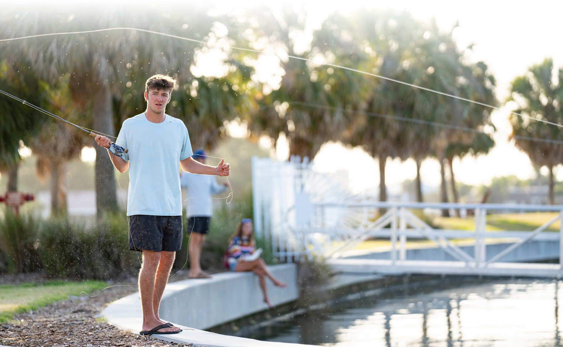 College student flyfishing along seawall as his friends watch