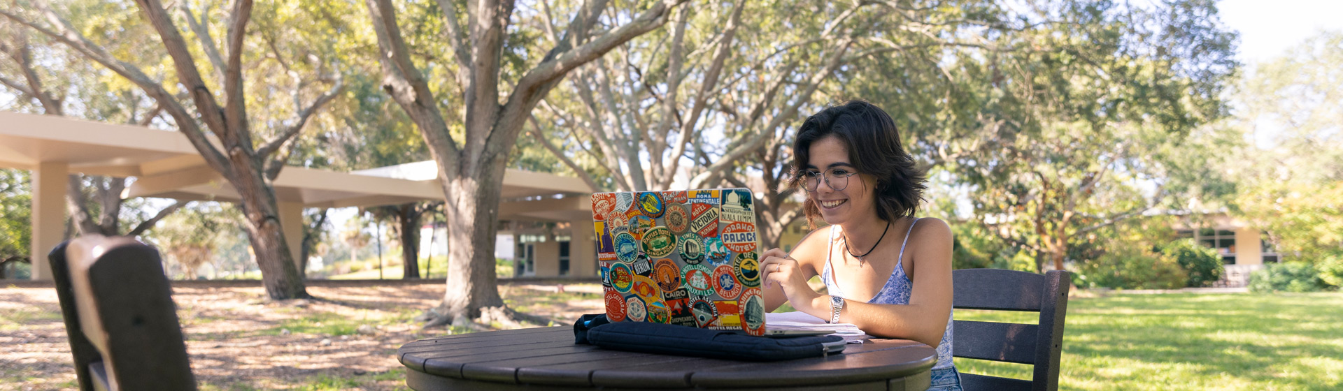student wearing glasses reads looks at laptop computer while seated outside
