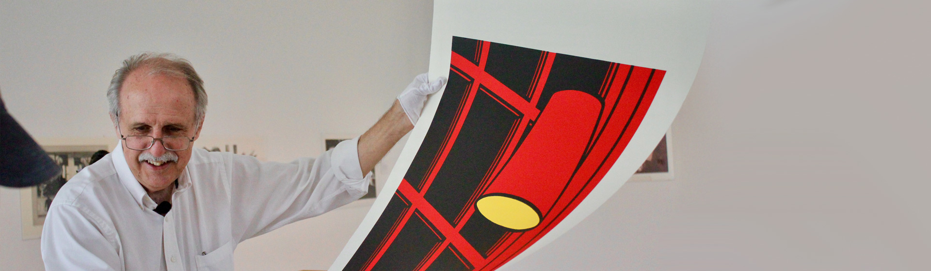 Professor in glasses and white gloves smiles as he holds up a print