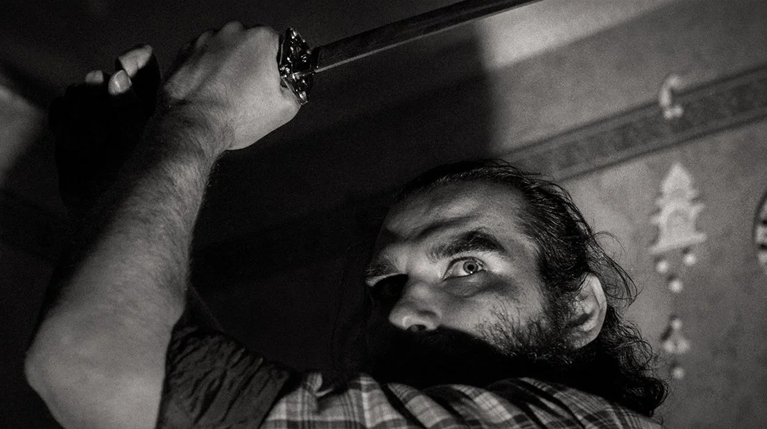 Man holding up sword over his head looking back to camera ominously