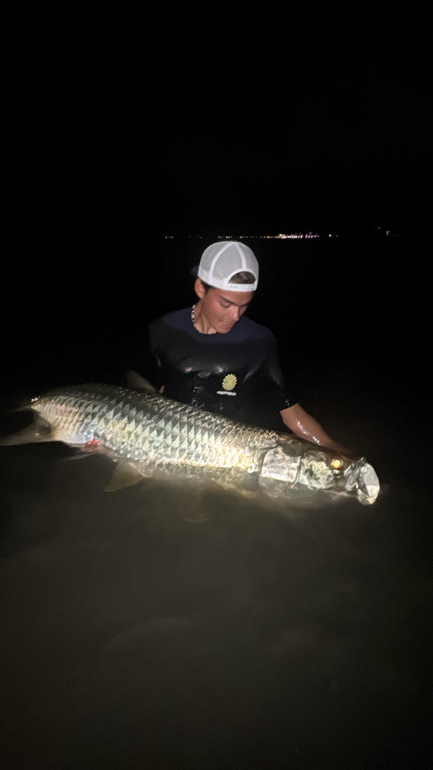 Student with baseball hat on backwards holding a tarpon in the water