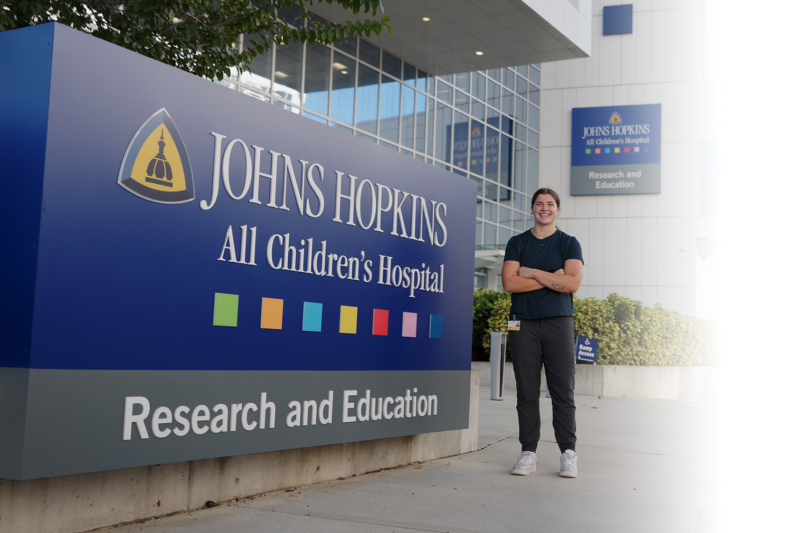 College student stands in front of a hospital with a sign that reads Johns Hopkins All Children's Hospital Research and Education